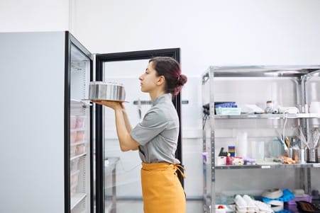 Une personne met un plat dans un réfrigérateur 