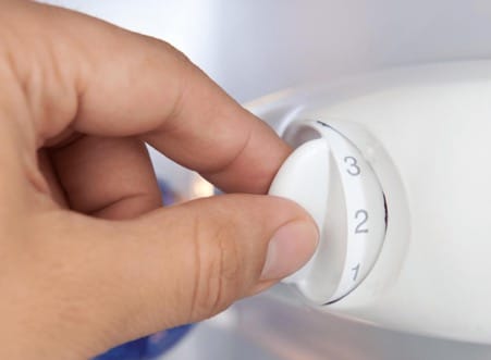 Une personne tourne le thermostat d'un frigo