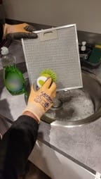 Une main gantée brosse le filtre métallique d'une hotte aspirante